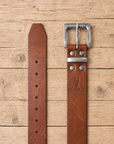 jeans belt made of full grain vegetal leather in chestnut brown tan colour with roller style metal buckle on a rustic wooden table