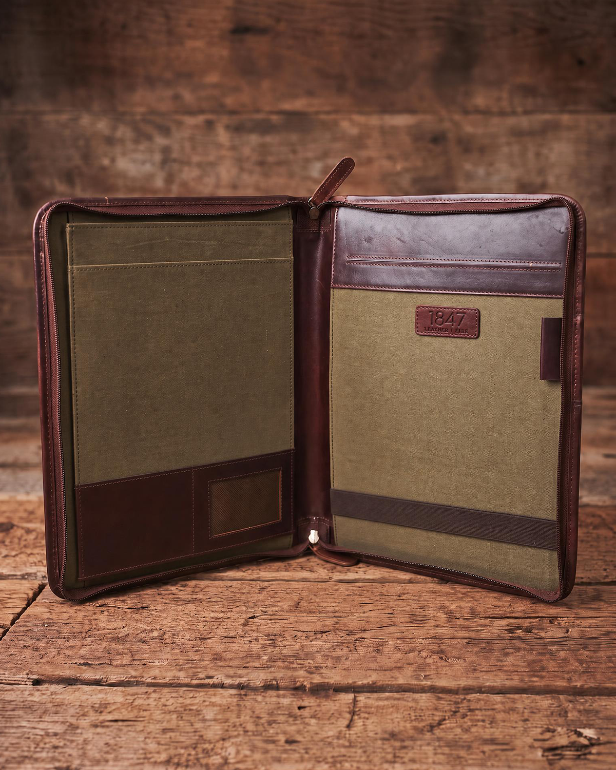 An open leather and canvas document organizer with interior pockets, shown on a rustic wooden surface against a wood plank background.