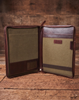 An open leather and canvas document organizer with interior pockets, shown on a rustic wooden surface against a wood plank background.
