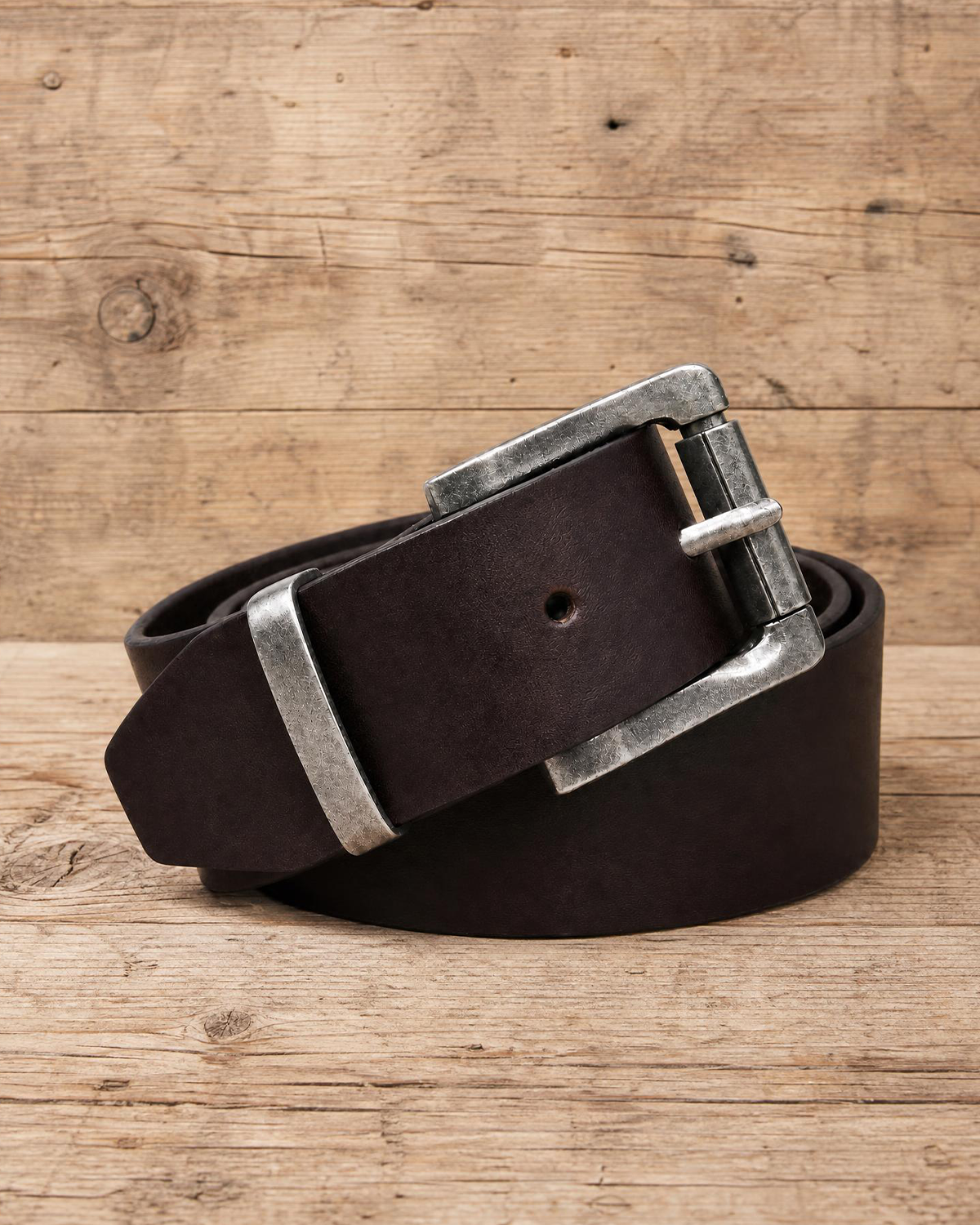 jeans belt made of full grain vegetal leather in deep/chocolate brown tan colour with roller style metal buckle on a rustic wooden table