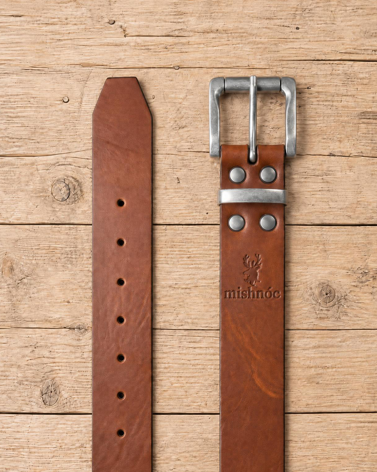 jeans belt made of full grain vegetal leather in chestnut brown tan colour with roller style metal buckle on a rustic wooden table