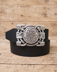 A black leather belt with an ornate silver-toned Celtic knot buckle, coiled on a rustic wooden surface.