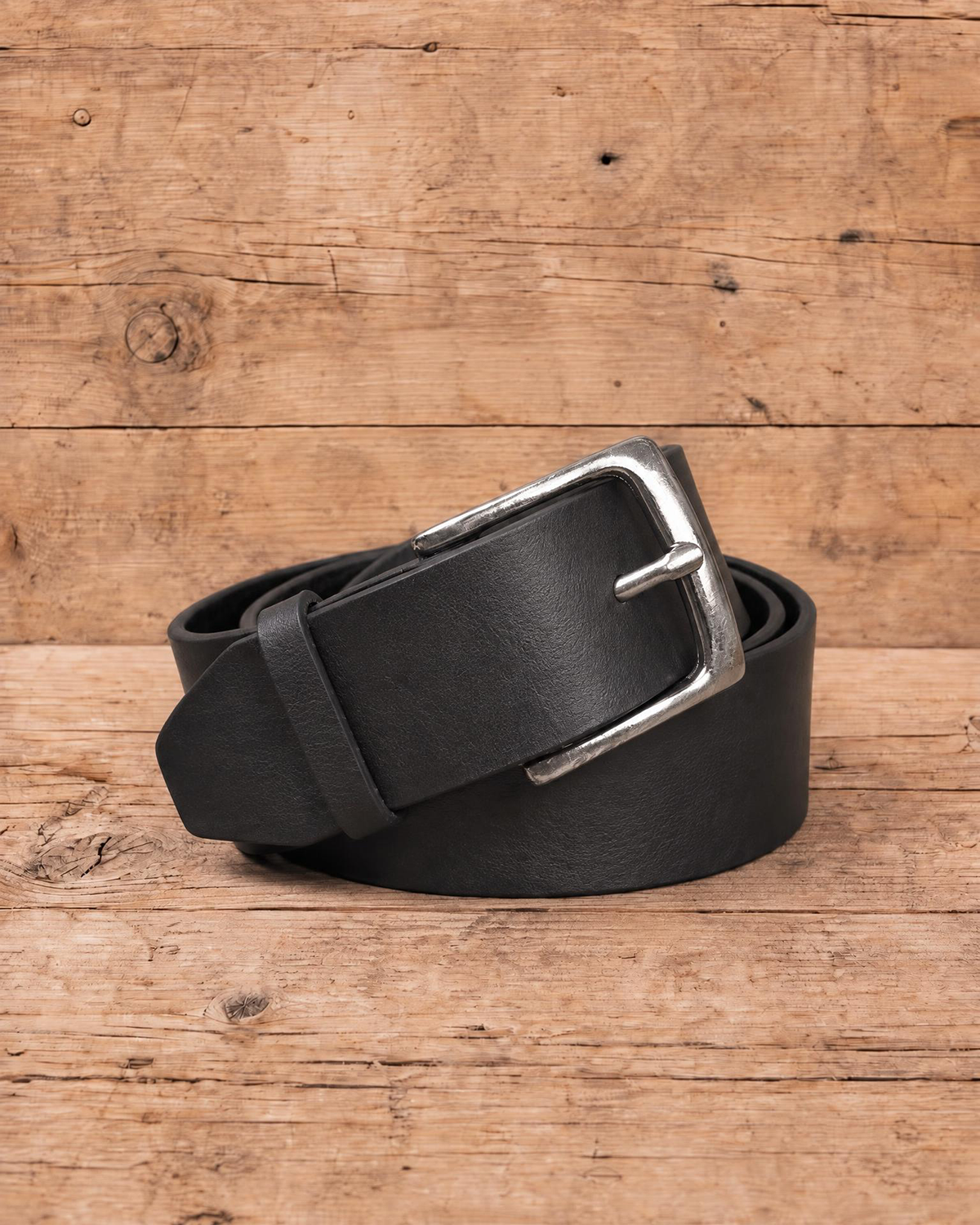 slim suit belt made of full grain vegetal leather in black colour with polished brass style metal buckle on a rustic wooden table