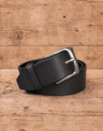 slim suit belt made of full grain vegetal leather in black colour with polished brass style metal buckle on a rustic wooden table