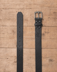 slim suit belt made of full grain vegetal leather in black colour with polished brass style metal buckle on a rustic wooden table