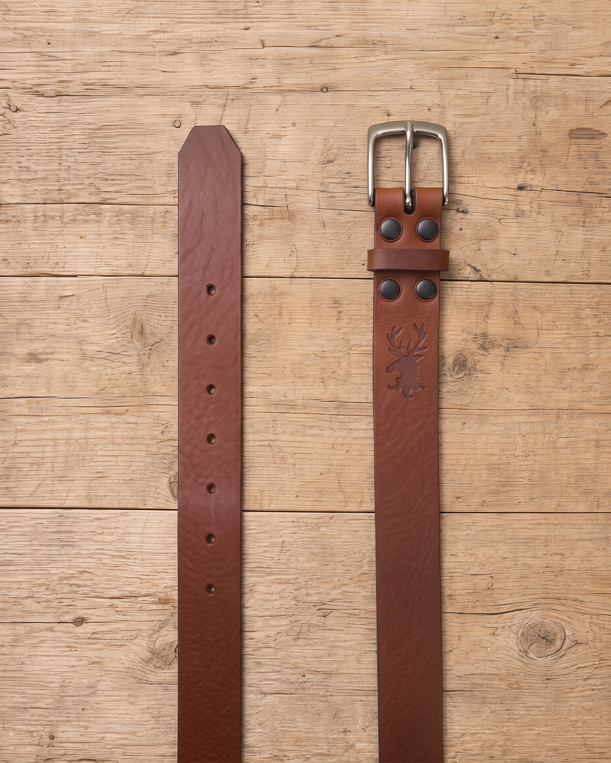 slim suit belt made of full grain vegetal leather in chestnut brown tan colour with polished brass style metal buckle on a rustic wooden table